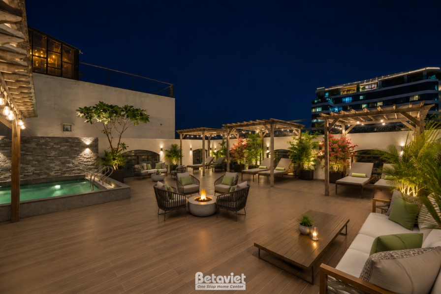 Sân thượng về đêm với bể bơi nhỏ dạng ngâm ốp đá, cạnh đó bố trí sofa ngoài trời đệm kem, bàn gỗ thấp và giàn pergola gỗ c…
